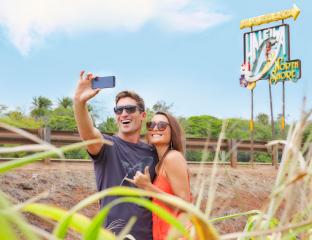 A couple taking a selfie in front of the Haleiwa Town sign