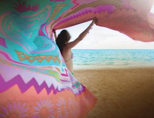 A woman on a beach waving a colorful sarong